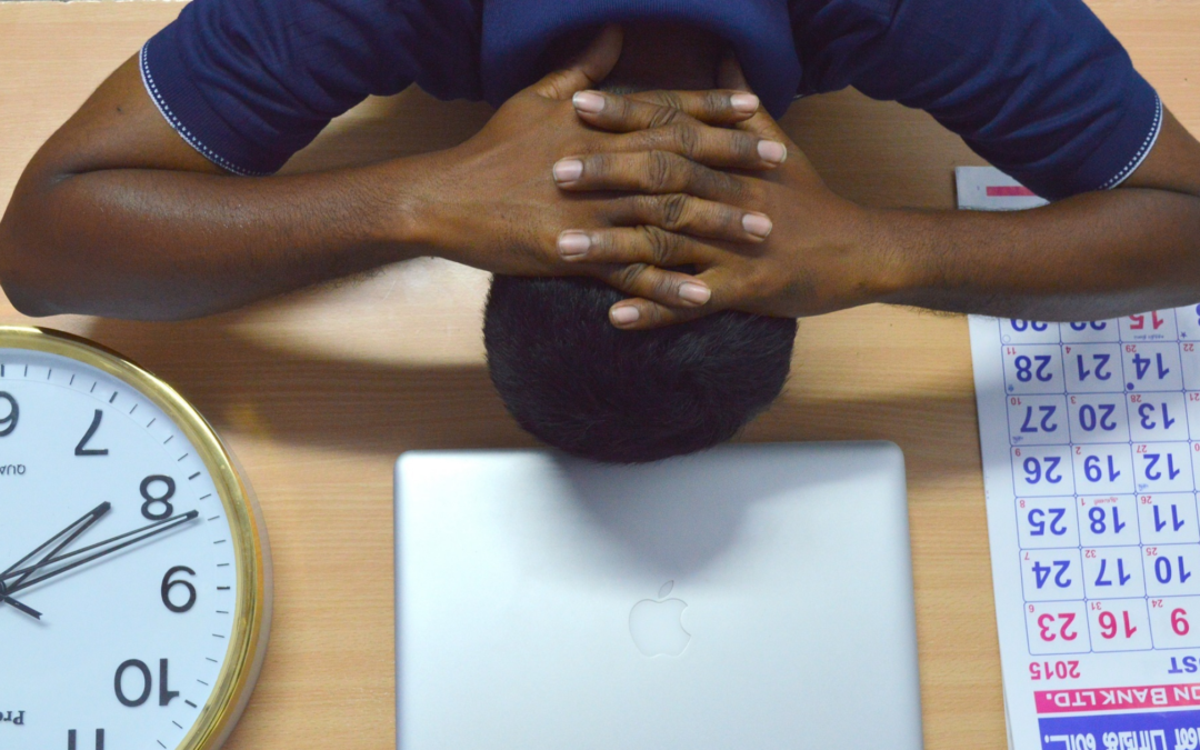 man with head on desk surrounded by clock and calendar 4 day work week